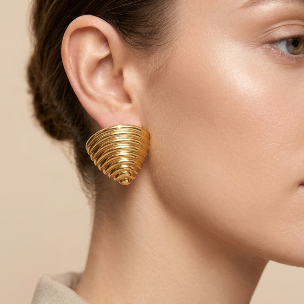 A model worn 18kt gold plated ribbed croissant style triangular studs on her ear.