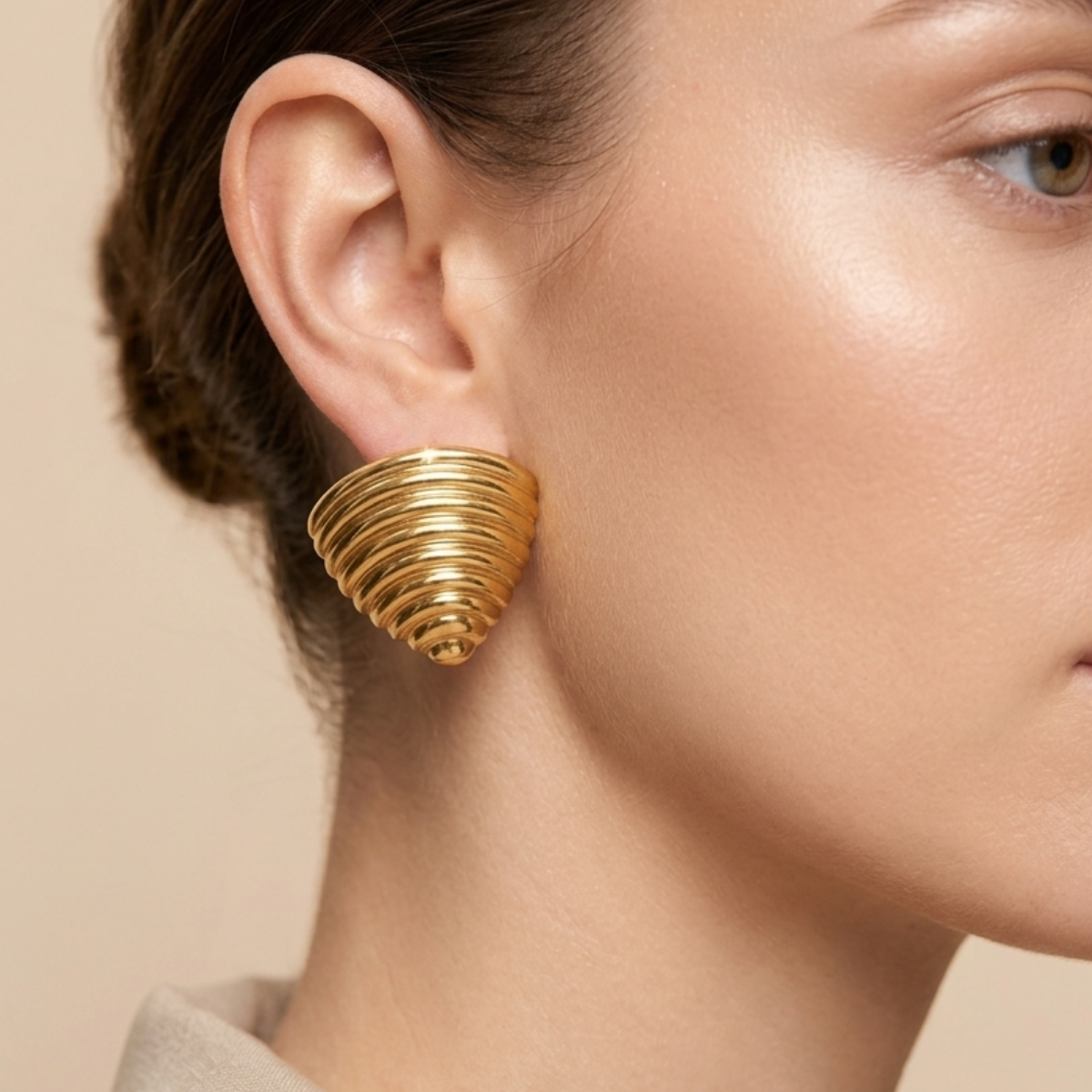 A model worn 18kt gold plated ribbed croissant style triangular studs on her ear.