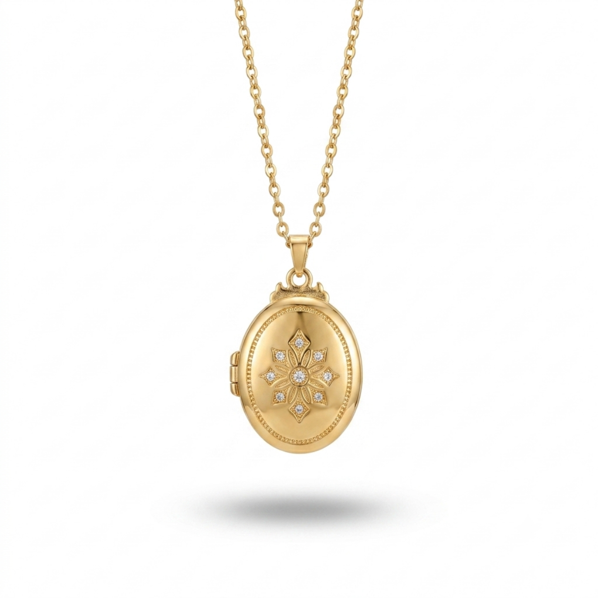 A gold oval locket necklace with a floral starburst design set with small clear stones in the center, hanging from a delicate gold chain against a white background.
