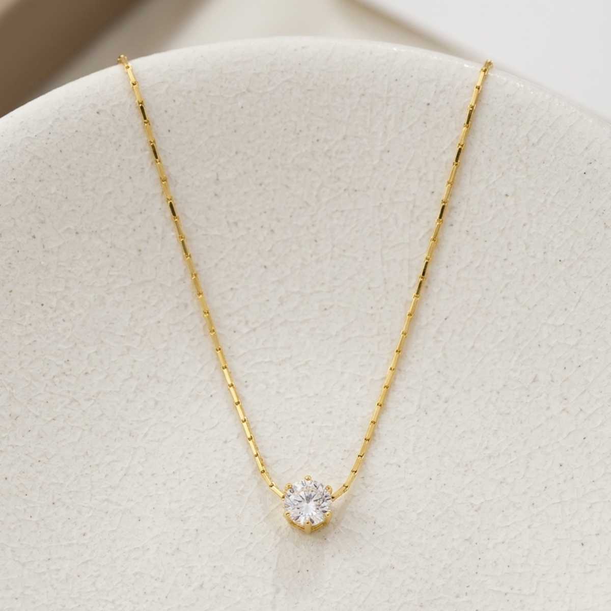Gold necklace with a diamond pendant on a light gray surface