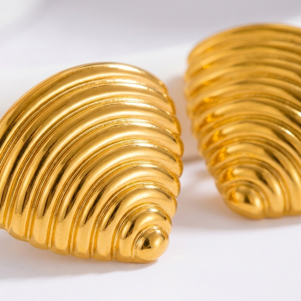 A close-up of 18kt gold plated ribbed croissant style triangular studs on white background.