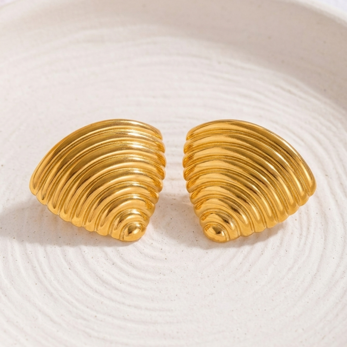 18kt gold plated ribbed croissant style triangular studs on white stone plate.