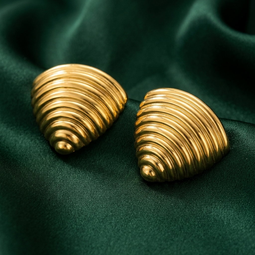 18kt gold plated ribbed croissant style triangular studs resting on smooth green fabric.