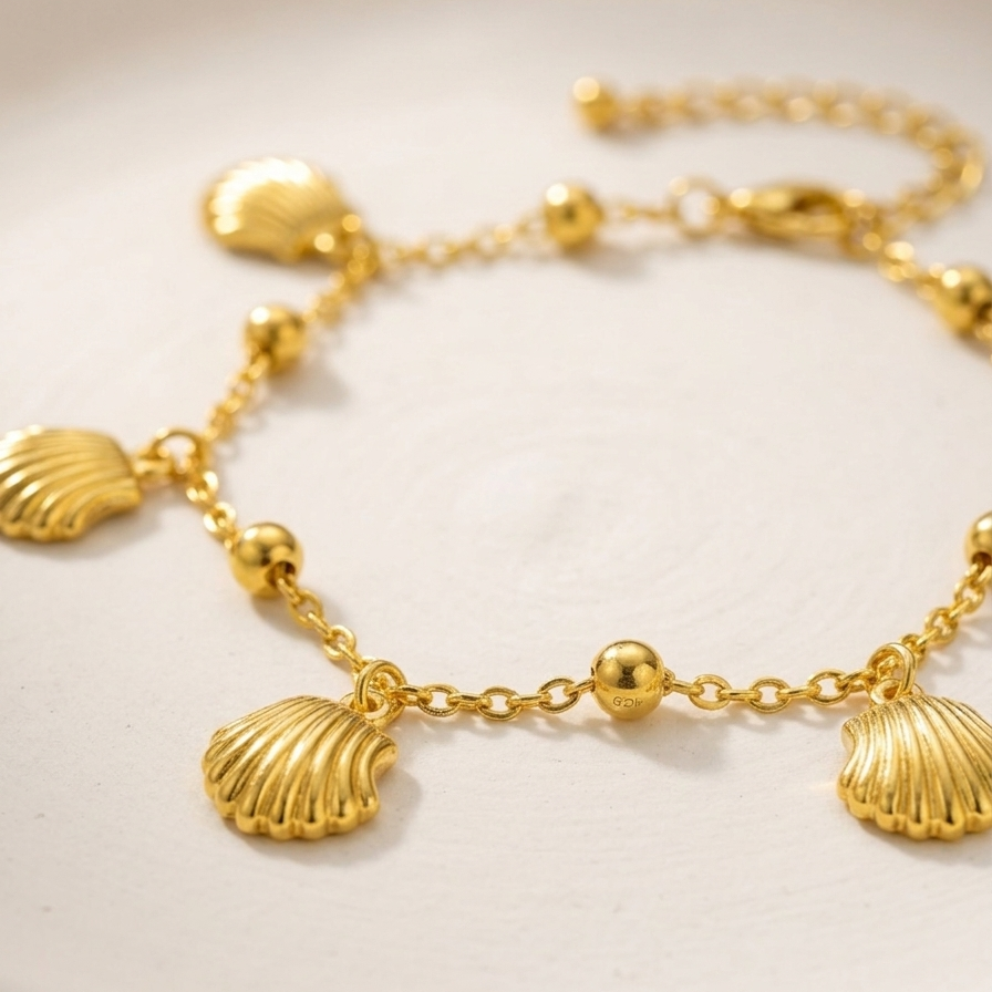 Close-up of 18kt gold plated bracelet with shell charms on a white plate.