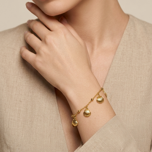 Woman wearing a 18kt gold plated bracelet with small charms against a neutral background.