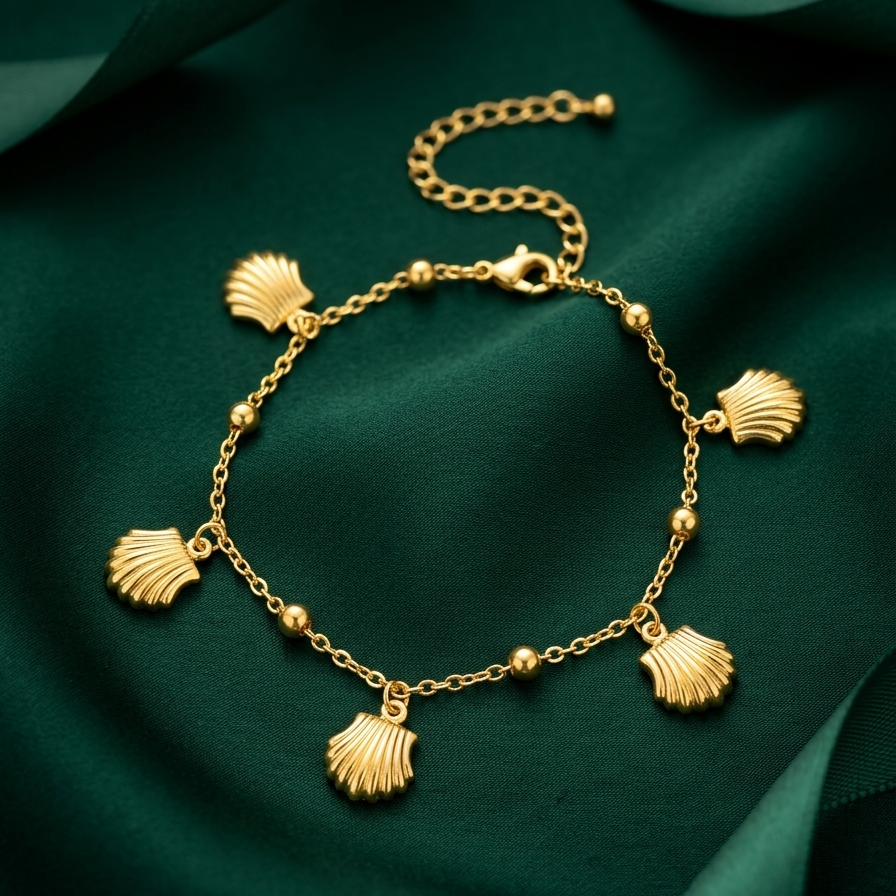 18kt gold plated Amalfi scallop bracelet with shell charms on a green fabric background.