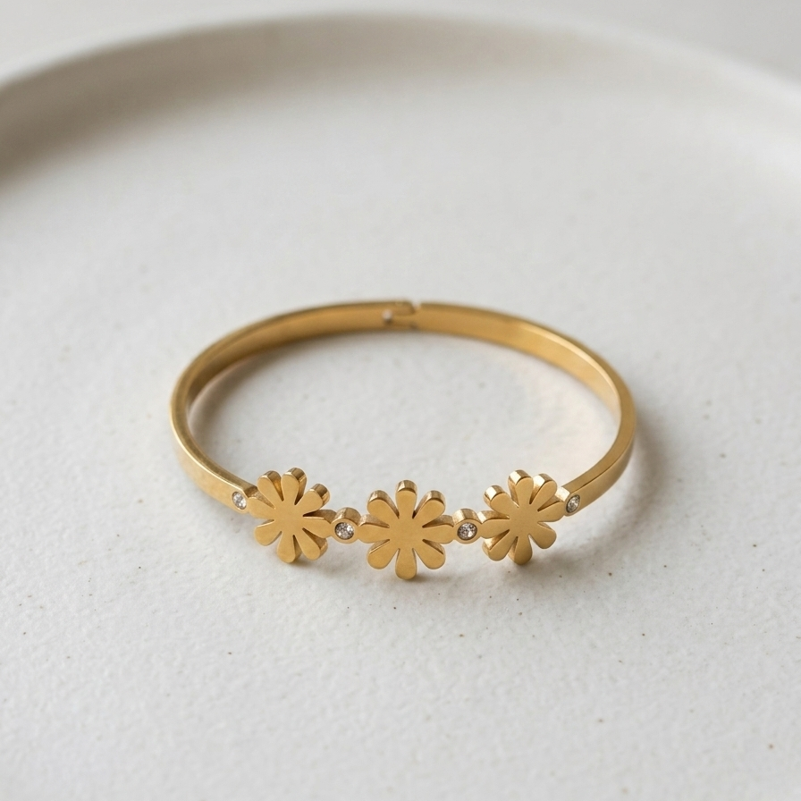18k gold plated minimalist bangle bracelet featuring three solid gold daisy motifs and tiny crystal accents, resting on a white plate.