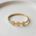 18k gold plated minimalist bangle bracelet featuring three solid gold daisy motifs and tiny crystal accents, resting on a white plate.