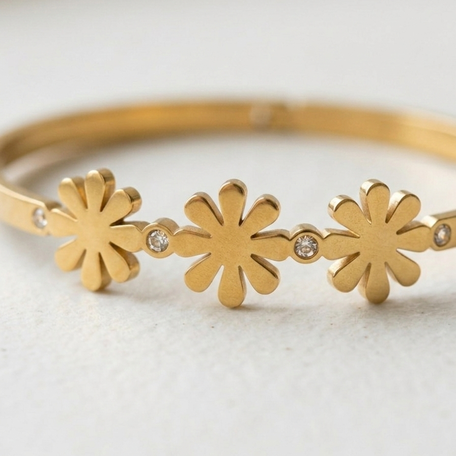 Close up of 18k gold plated minimalist bangle bracelet featuring three solid gold daisy motifs and tiny crystal accents, resting on a white plate.