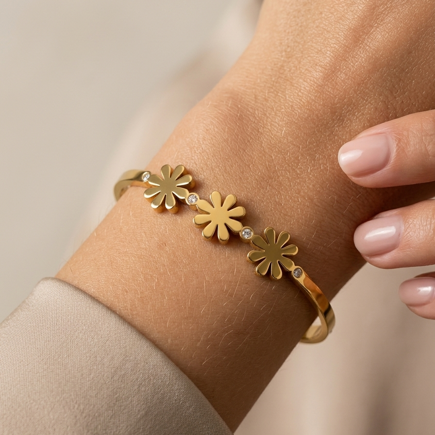 18k gold plated minimalist bangle bracelet featuring three solid gold daisy motifs and tiny crystal accents, resting on a white plate.on a wrist against a neutral background