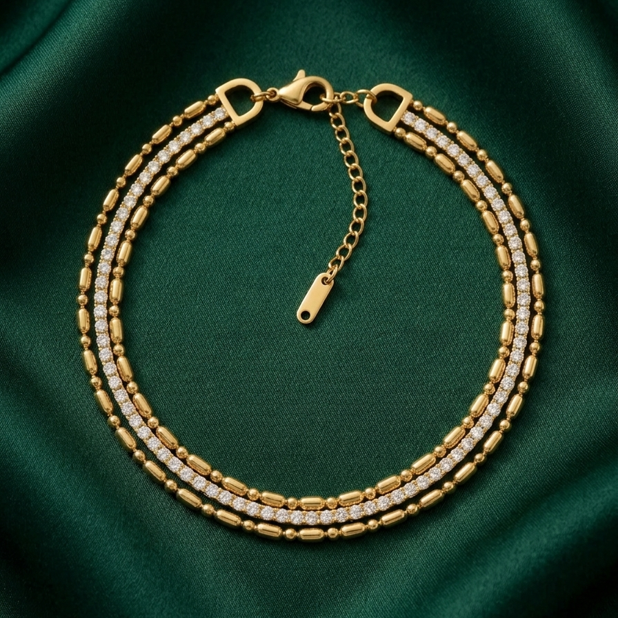 wrist wearing a layered 18k gold plated bracelet featuring delicate gold beads and a row of sparkling CZ diamonds on a green fabric background