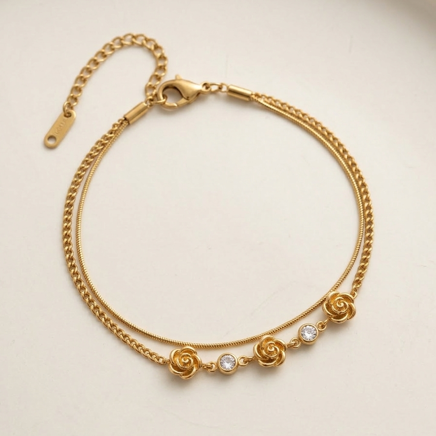 18k gold plated double chain bracelet featuring sculpted rose charms and crystal accents, resting on a matte white surface.