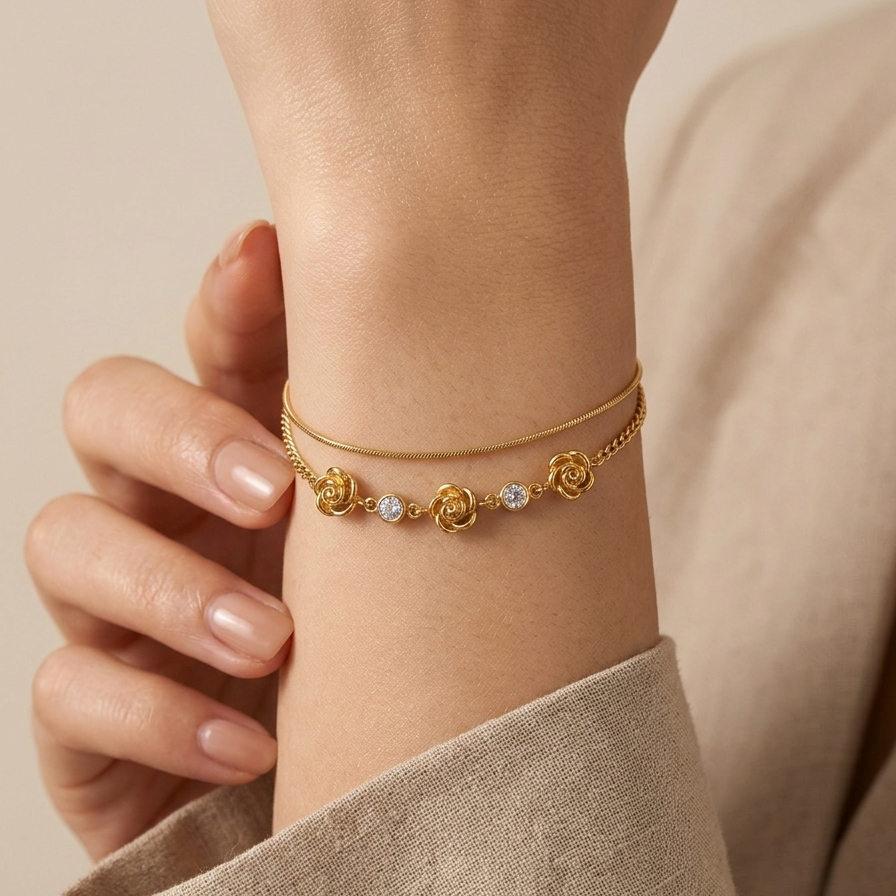 18k gold plated double chain bracelet featuring sculpted rose charms and crystal accents, resting on a matte white surface.