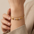 18k gold plated double chain bracelet featuring sculpted rose charms and crystal accents, resting on a matte white surface.