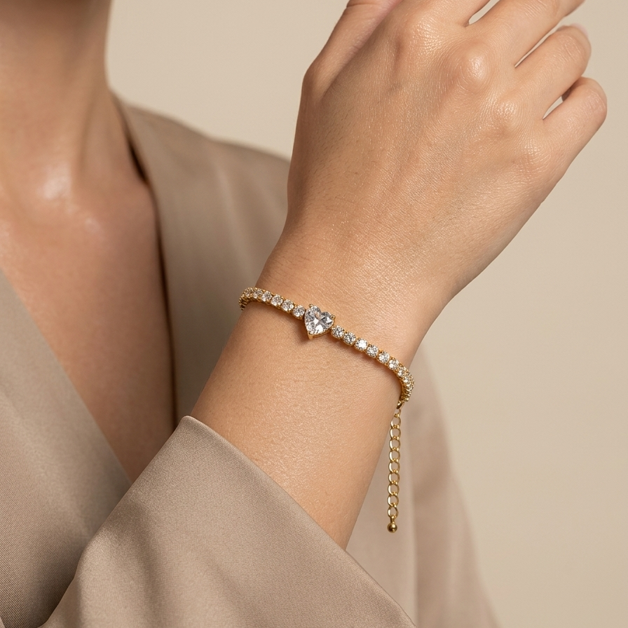 Close-up of a hand wearing a 18k gold plated tennis bracelet featuring a row of CZ diamonds and a prominent heart-shaped center diamond on a beige background