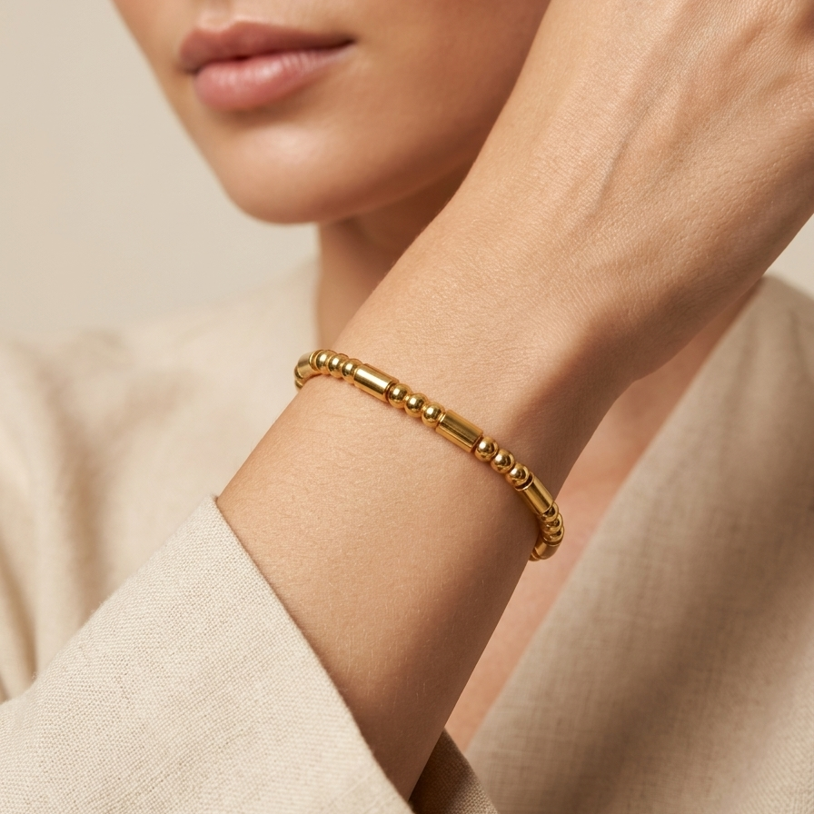 Close-up of a person wearing a 18k gold plated bracelet featuring a minimalist pattern of alternating polished gold spheres and sleek cylinder links on a neutral background
