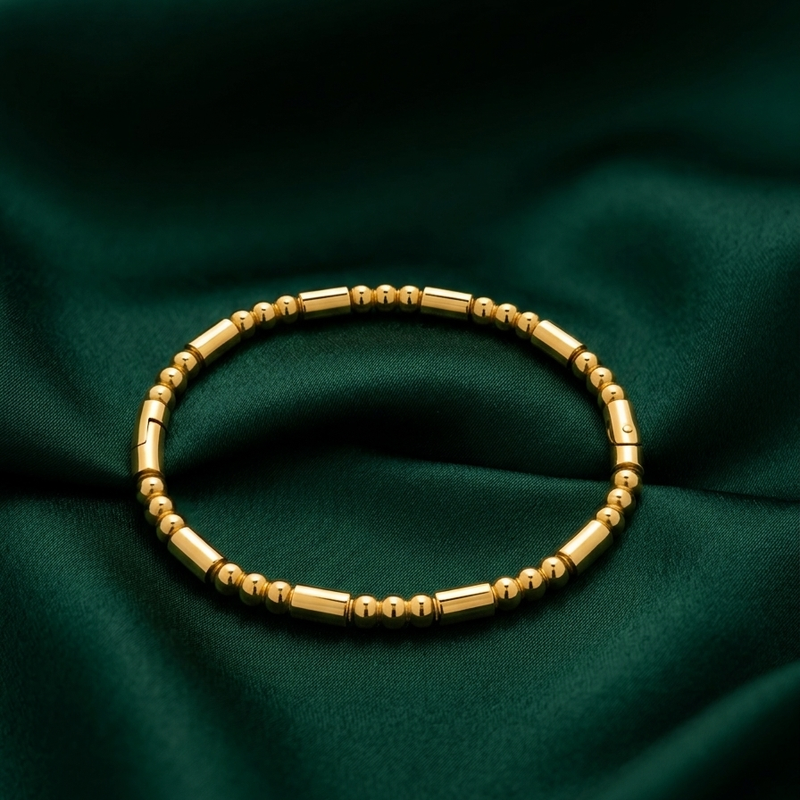 18k gold plated bracelet featuring a minimalist pattern of alternating polished gold spheres and sleek cylinder links on a dark green fabric background