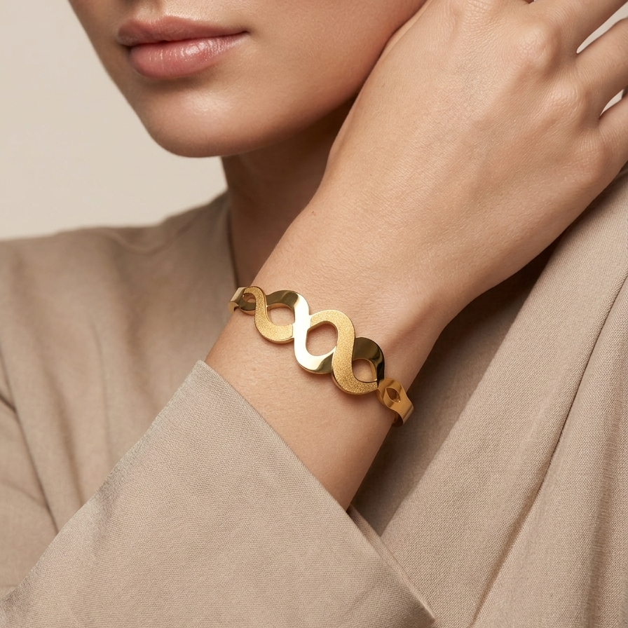 18k gold plated bangle bracelet featuring an infinity wave cutout design with alternating polished and frosted gold textures on a person's wrist with a neutral background