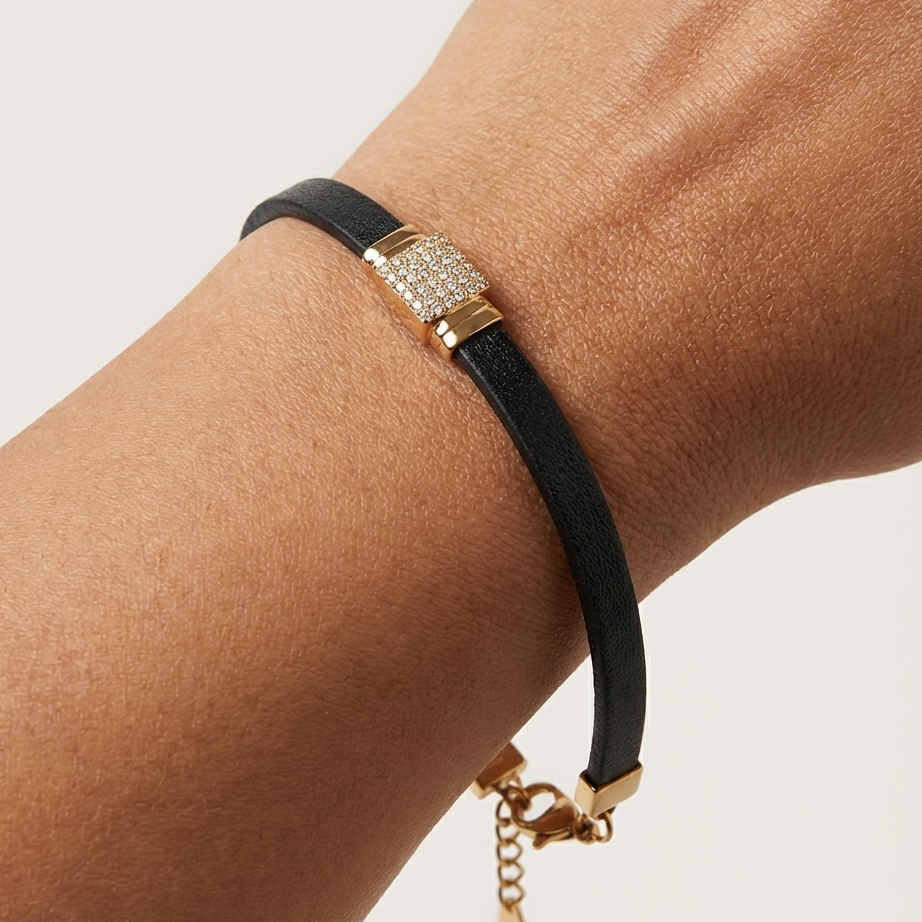 A model's wrist wearing a sporty black ribbed bracelet featuring a bold, rectangular 18k gold plated clasp covered in pave CZ diamonds.