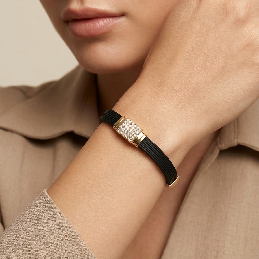 A model's wrist wearing a sporty black ribbed bracelet featuring a bold, rectangular 18k gold plated clasp covered in pave CZ diamonds.