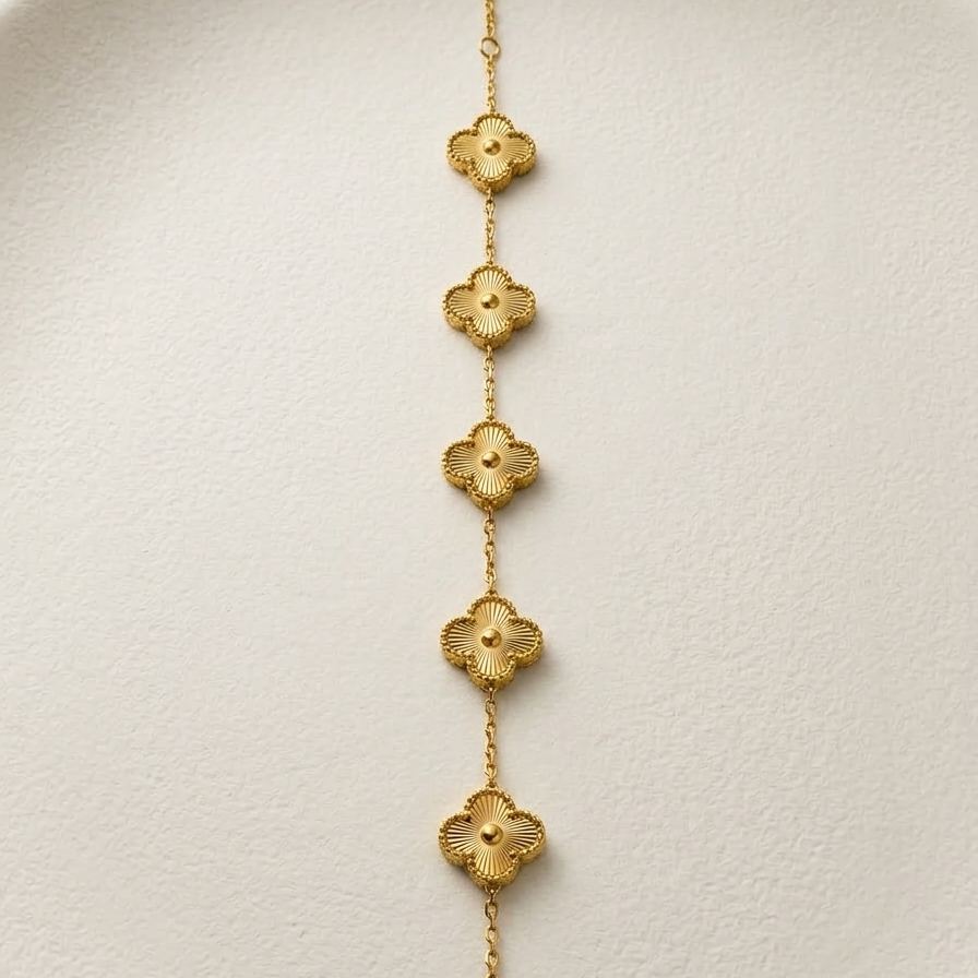 18k gold plated delicate chain bracelet featuring five textured four-leaf clover motifs, resting vertically on a matte white surface.