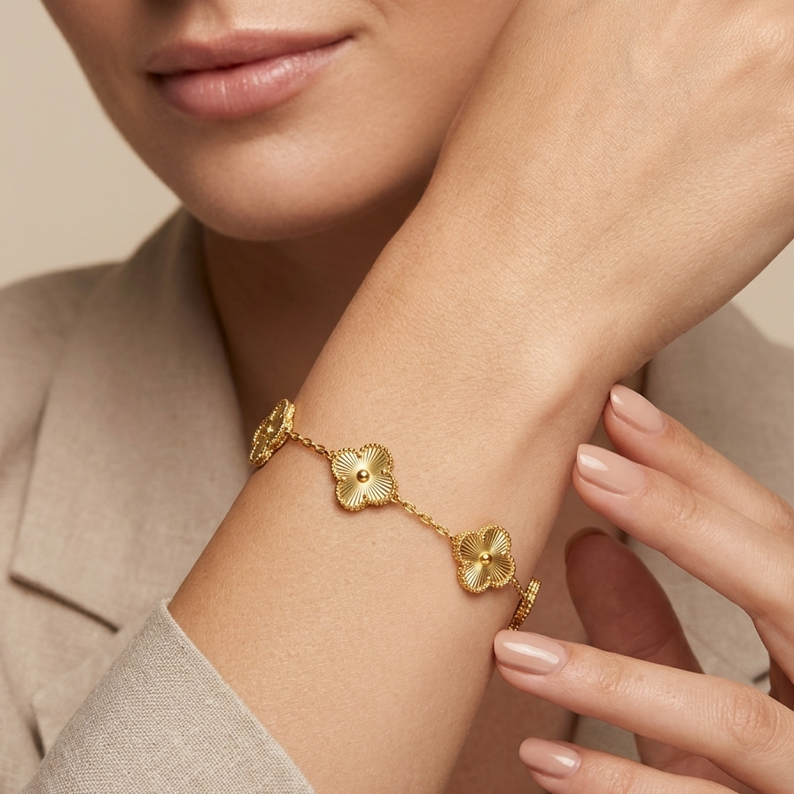 Close-up of a woman's arm wearing a 18k gold plated delicate chain bracelet featuring five textured four-leaf clover motifs, resting vertically on a matte white surface against a neutral background.