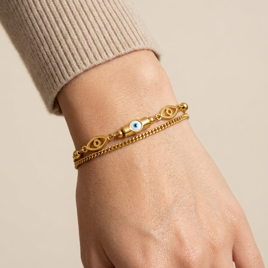18k gold plated double chain bracelet featuring a central blue and white evil eye charm flanked by golden eye motifs and beads on a wrist against a beige background