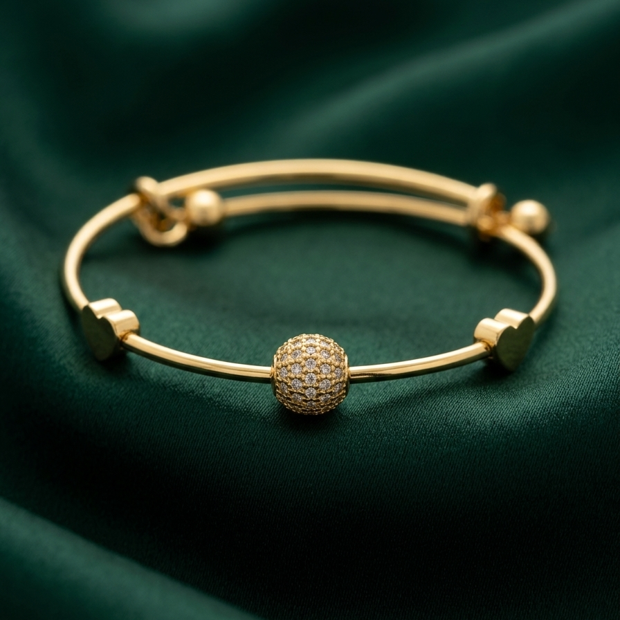 18k gold plated adjustable sliding bangle bracelet featuring a central sphere covered in pave CZ diamonds and two small gold heart accents on a green fabric background