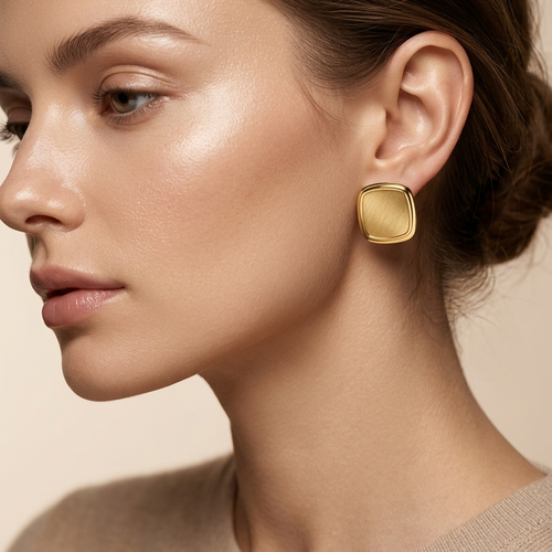 Close-up of a woman wearing 18kt gold plated square studs with a neutral background