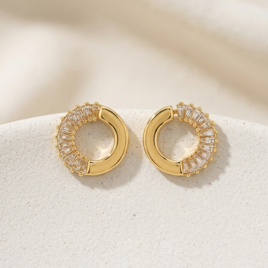 Pair of 18k gold plated open hoop earrings featuring baguette cut CZ diamonds on one half and smooth gold on the other.