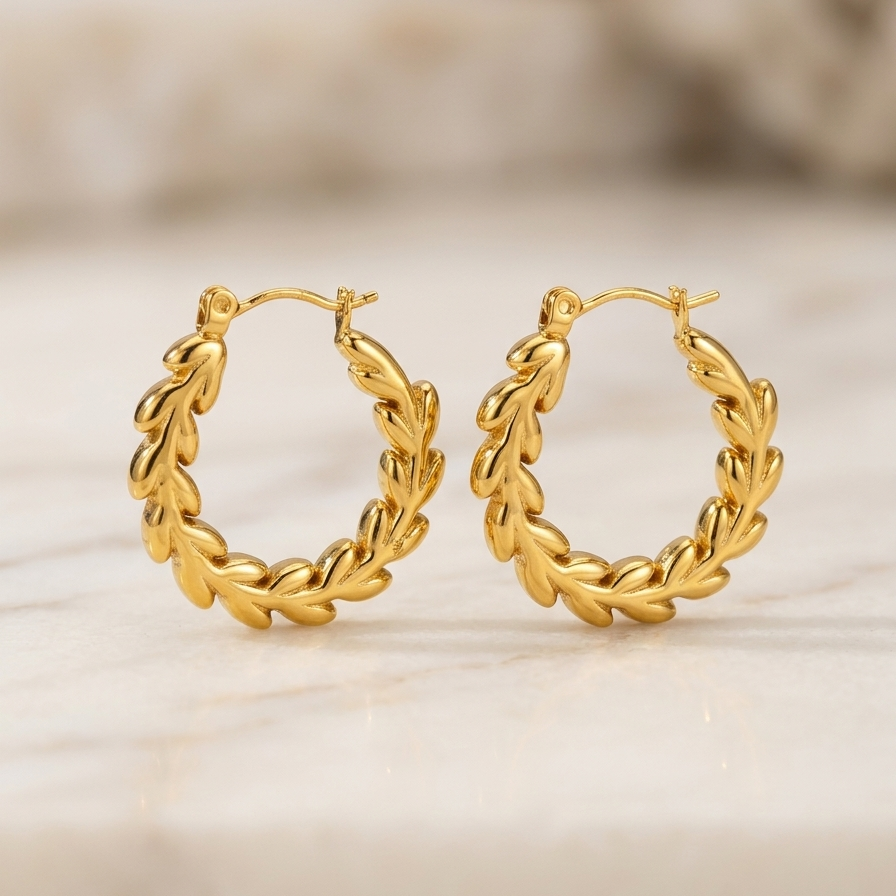 18k gold plated hoop earrings with an intricate braided vine and leaf texture, sitting on a binge surface.