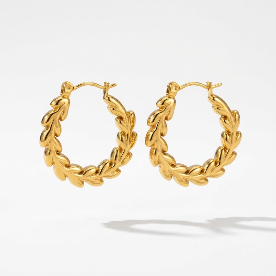 Close up of 18k gold plated hoop earrings with an intricate braided vine and leaf texture, floating in with white background.