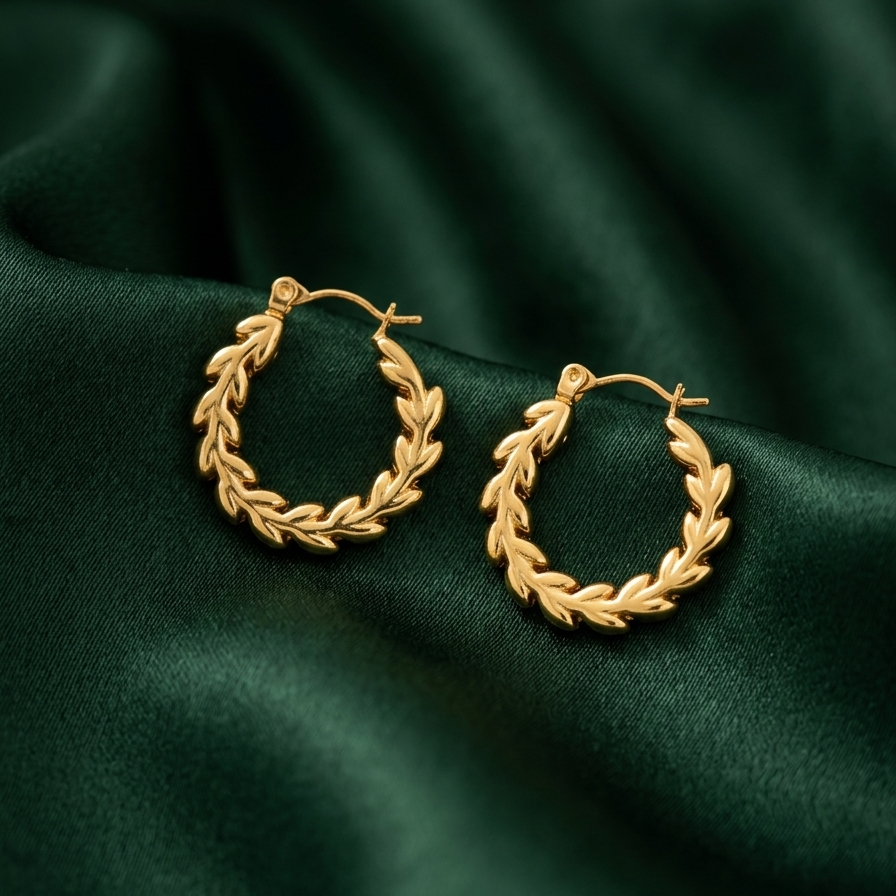18k gold plated hoop earrings with an intricate braided vine and leaf texture, sitting on a deep green silk fabric.