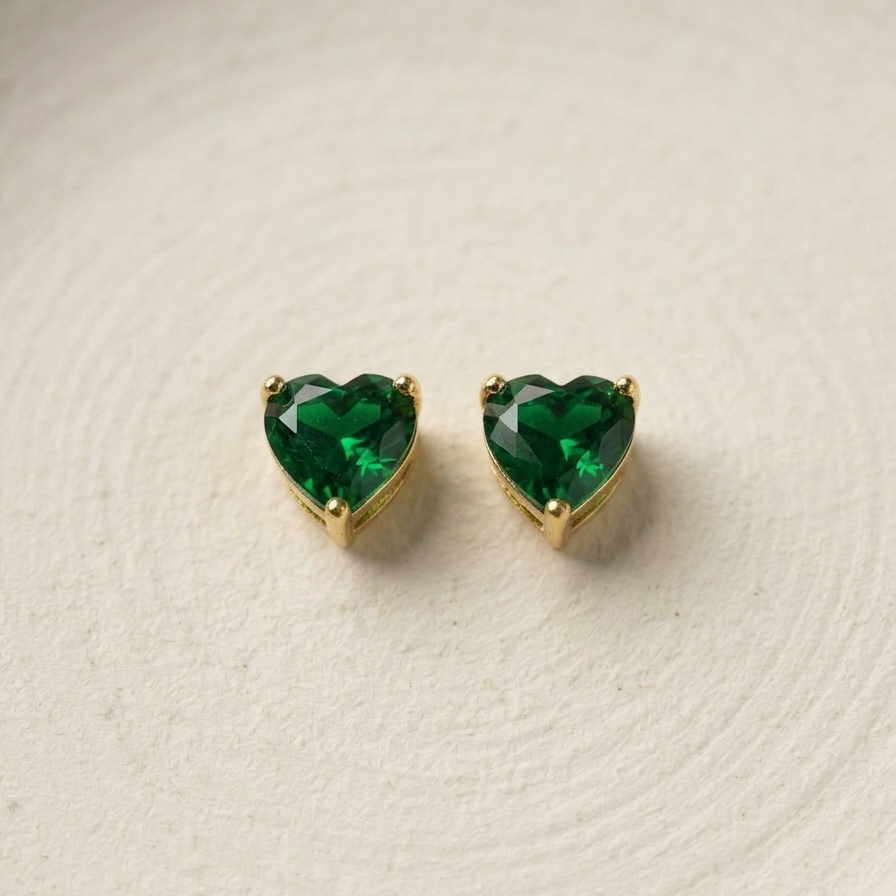 Heart-shaped green gemstone earrings on a textured beige background
