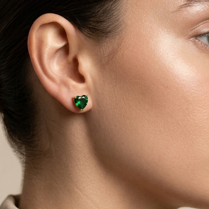 Close-up of a person wearing green heart-shaped earrings on a neutral background