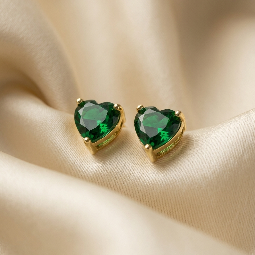 Heart-shaped green gemstone earrings with gold settings on a beige fabric background