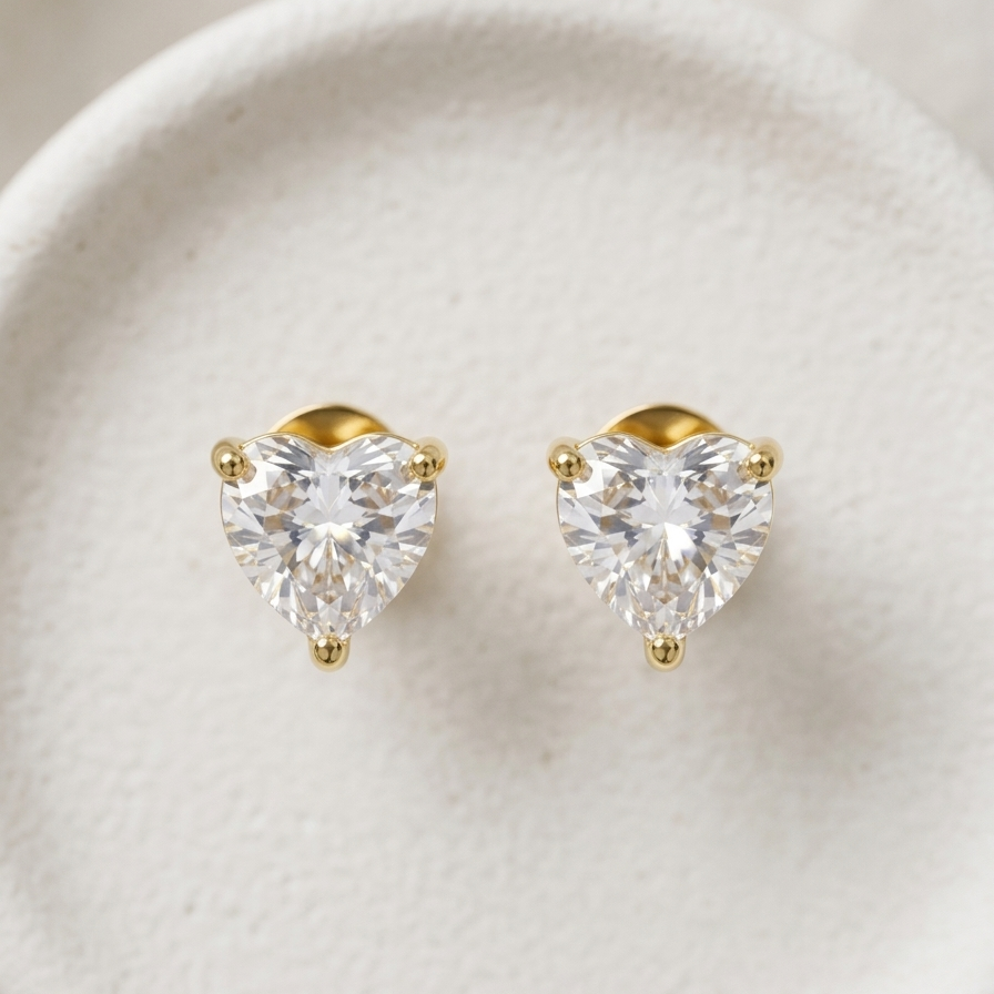 18k gold plated stud earrings featuring a clear, sparkling heart-shaped diamond on a dark marble surface.