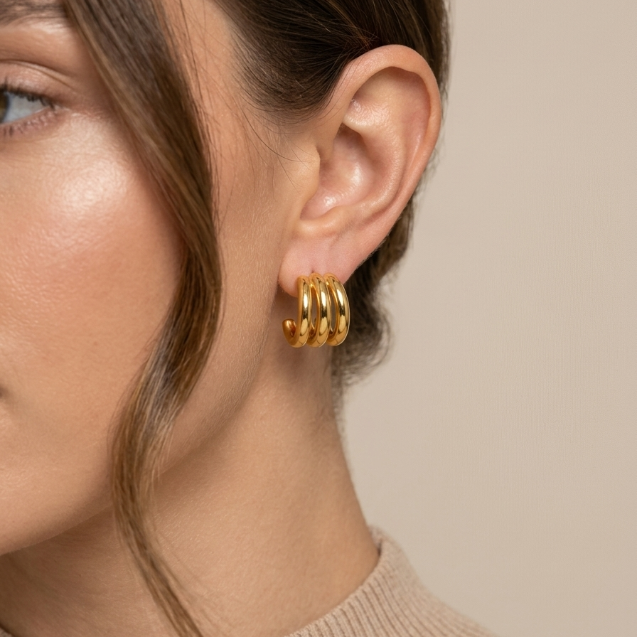 Close-up of a person wearing gold hoop earrings with a neutral background