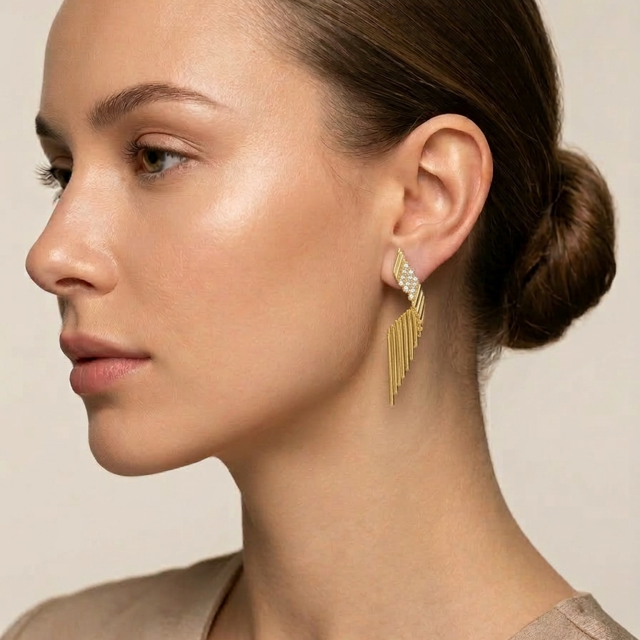 Woman wearing Pair of large 18k gold plated statement drop earrings with a ribbed wing texture and CZ diamond accents at the top. with a neutral background