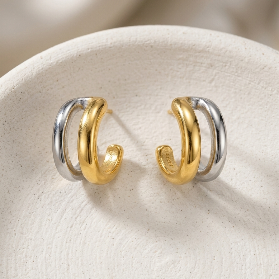 double hoop earrings, featuring one gold band and one silver band intertwined, resting on a textured white surface.
