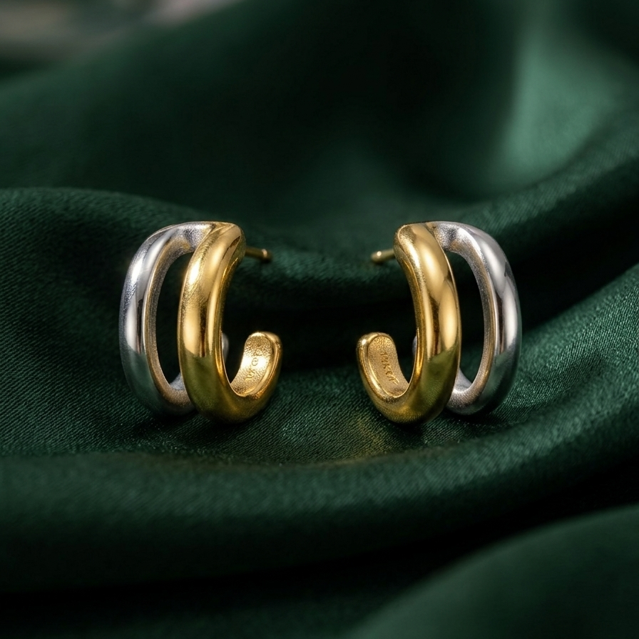  double hoop earrings, featuring one gold band and one silver band intertwined, resting on a green fabric background