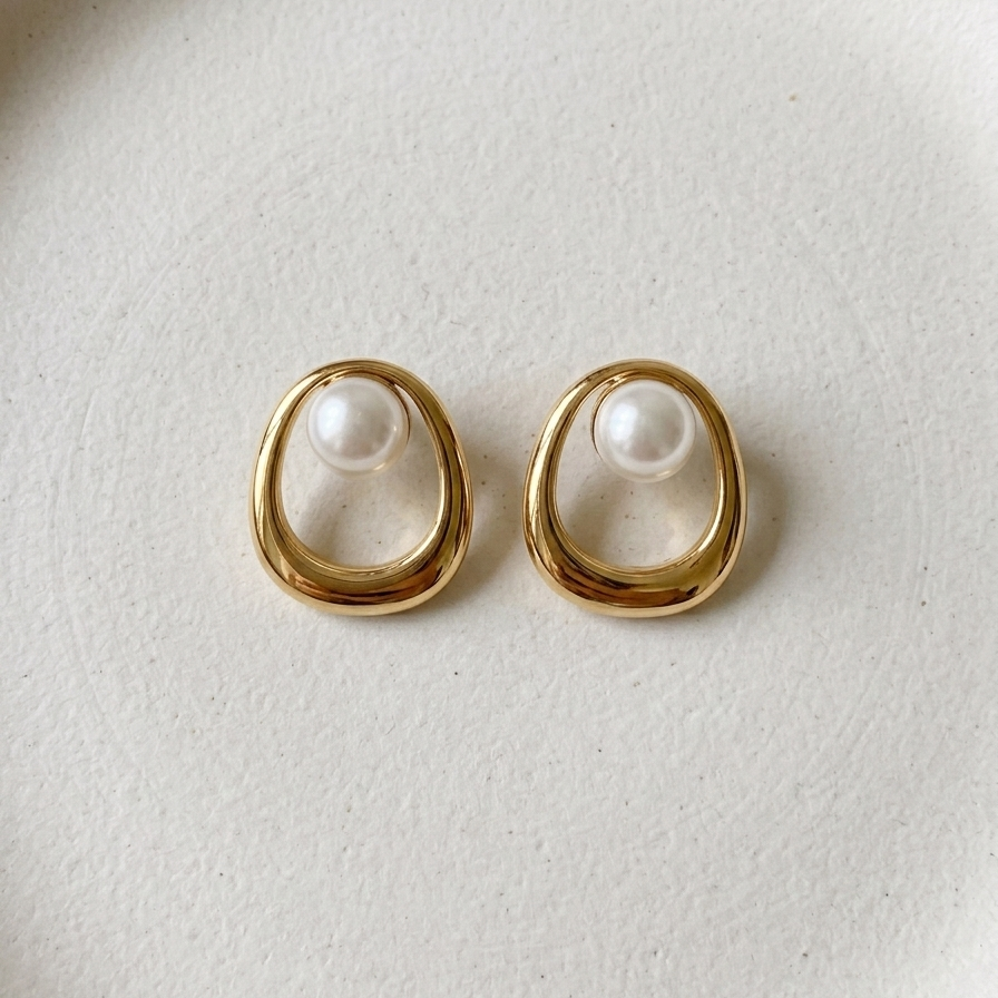 Pair of 18k gold plated stud earrings featuring an open oval design with a single white pearl resting on the white plate.