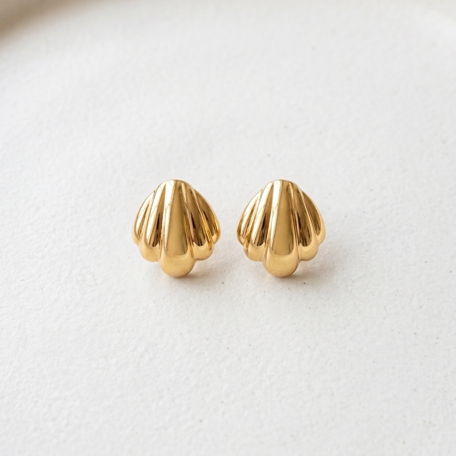18k gold plated stud earrings shaped like polished minimalist scallop seashells, resting on a matte white ceramic dish.