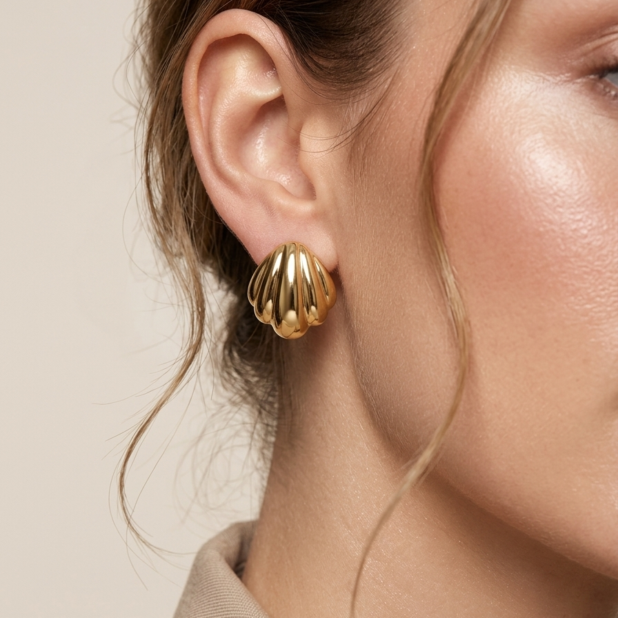18k gold plated stud earrings shaped like polished minimalist scallop seashells worn by a person with a neutral background.