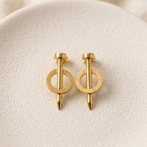 Pair of 18k gold plated statement drop earrings featuring an industrial nail design piercing through a circular halo with screw details, resting on a ceramic surface.