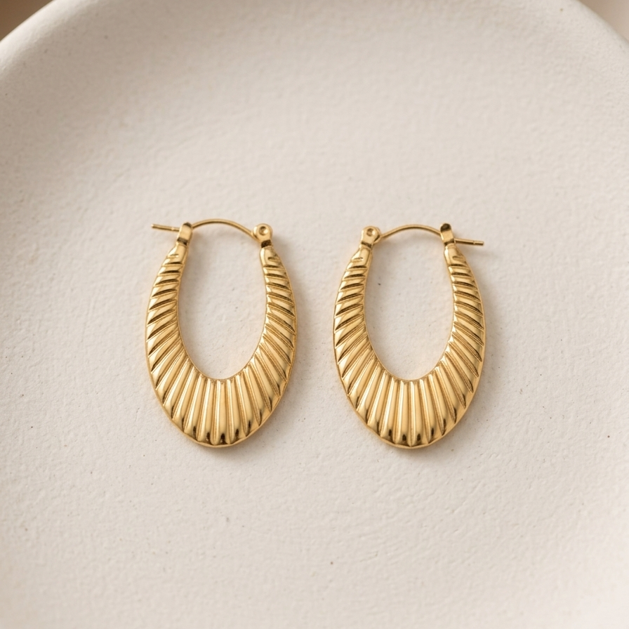 18k gold plated elongated oval hoop earrings featuring a ribbed croissant texture, resting on a matte white plate.
