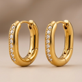 Close up of 18k gold plated oval huggie hoop earrings featuring a center row of sparkling CZ diamonds.