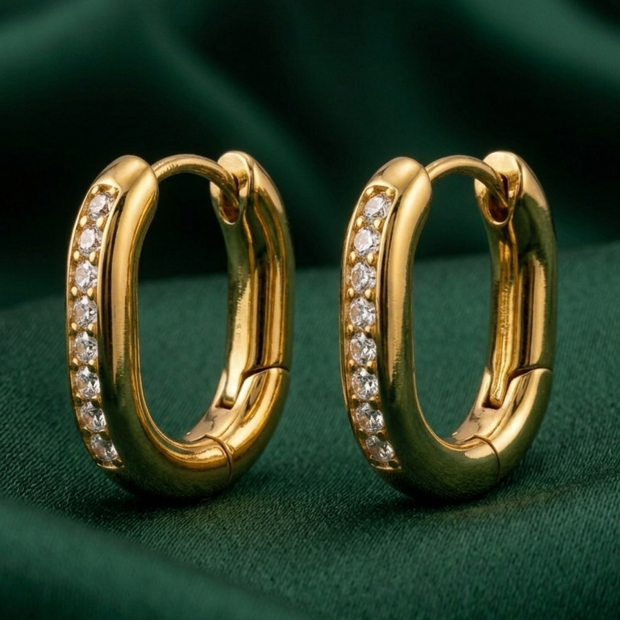 Pair of 18k gold plated oval huggie hoop earrings featuring a center row of sparkling CZ diamonds on a green fabric background