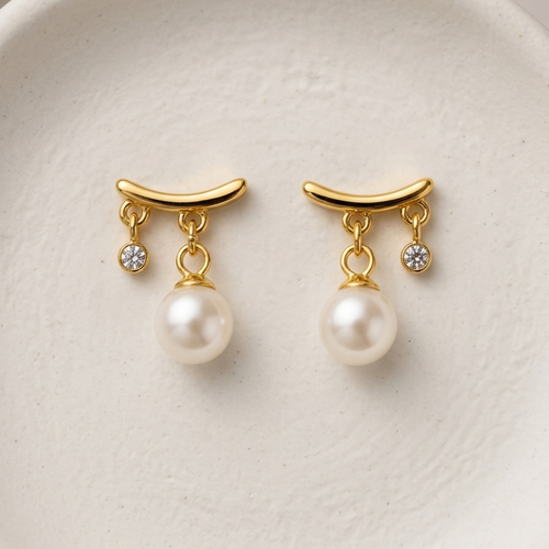 18k gold plated stud earrings featuring a curved gold bar with a dangling white pearl and a smaller dangling CZ diamond, on a white ceramic surface.