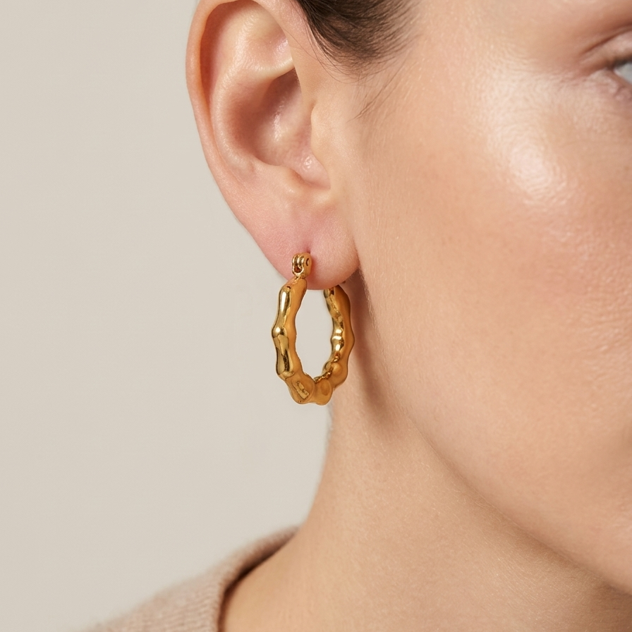 Pair of 18k gold plated mini hoop huggie earrings featuring a sculpted, textured bamboo design worn by a person on a neutral background